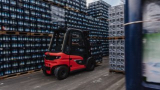 Le chariot électrique Fenwick X30 transporte des caisses de boissons dans une allée étroite d’un entrepôt extérieur.